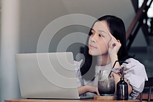 Thinking women with white laptop computer in co-working space