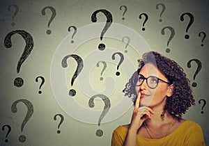 Thinking young business woman in glasses looking up at many question marks