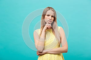 Thinking young confident woman in yellow dress looking up isolated on blue background