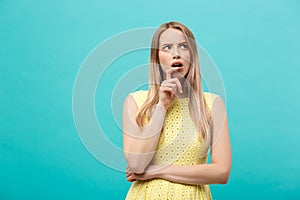 Thinking young confident woman in yellow dress looking up isolated on blue background