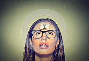 Thinking young woman with sand clock sign sticker on her forehead