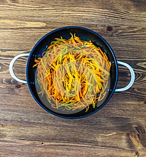 Thinly cut thin strips of carrots. fried and stewed carrot spaghetti in a pan on a wooden table