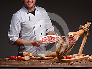 Smiling happy chef is holding a plate with thinly sliced jamon