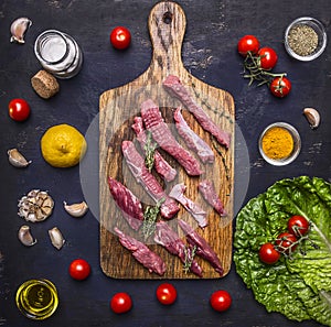 Thinly sliced lamb with garlic on a cutting board with a knife for meat, butter and salt, lettuce on wooden rustic background top