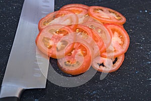 Thinly sliced plummy tomatoes on black cutting board