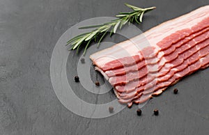 Thinly sliced strips of bacon lie on a dark slate background