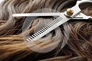 Thinning scissors on brown wavy hair, closeup.