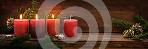 Third Advent, three of four red candles are lit with a flame, fir branches and Christmas decoration on dark rustic wood, wide