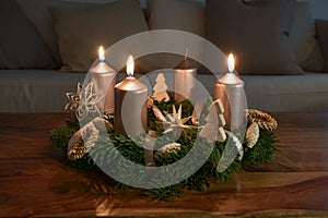 Third Advent with three lit golden candles on an Advent wreath with natural Christmas decoration on a wooden coffee table, copy