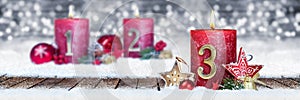 third sunday of advent red candle with golden metal number one on wooden planks in snow front of silver bokeh background