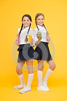 Thirst and dehydration. Healthy nutrition. Schoolgirls holding juice bottle on yellow background. Quenching thirst