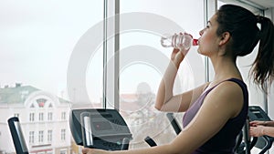 Thirst quenching into gym, girl runs on sports simulator and drinks water from bottle