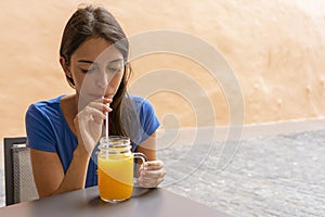 Thirst Teen smiling by the pleasure of a refreshing orange juice. Girlfriend sitting relaxing drinking a smoothie by plastic straw