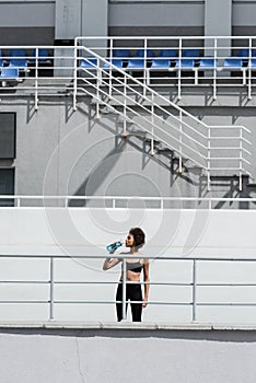 thirsty african american sportswoman drinking water