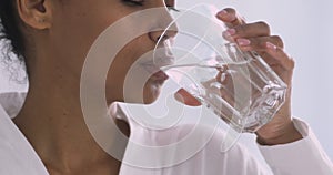 Thirsty african woman holding glass drinking water in morning, closeup