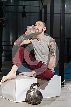 Thirsty armless young man drinking water on a pedestal next to a kettlebell