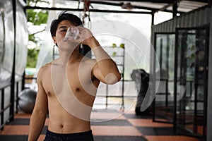 Thirsty Asian fitness man drinki water in gym