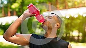 Thirsty black man drinking water from sports bottle after his training at park