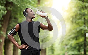 Thirsty black sportsman drinking water, jogging at park