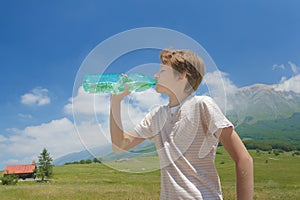 Thirsty boy drinking clear water from battle in his hands high in Alps