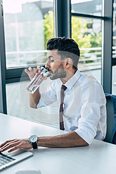 thirsty businessman drinking water while using laptop.