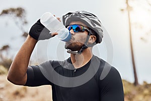 Thirsty cyclist taking a break and drinking water from a bottle. Fit young man wearing glasses and a helmet while