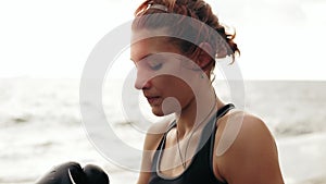 Thirsty female boxer in gloves taking a break drinking from the water bottle after training. Beautiful woman training by