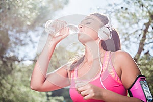 Thirsty female jogger drinking fresh water and listening music