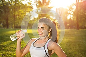 Thirsty fitness girl holding bottle of water in park.
