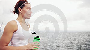 Thirsty fitness woman resting taking a break with water bottle drinking after training. Beautiful woman training by the