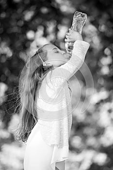 Thirsty girl drink water from bottle on natural background. Little child drink fresh water. Thirst and dehydration