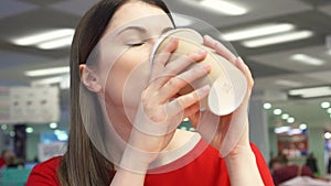 Thirsty girl drinking coffee from paper cup at fast food restaurant on food court.