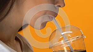 Thirsty girl drinking cold fizzy beverage from plastic cup with straw, close up