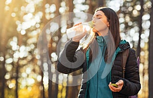 Thirsty girl drinking water while hiking by forest