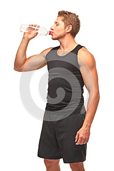 Thirsty handsome muscular young sportsman drinking water after hard workout