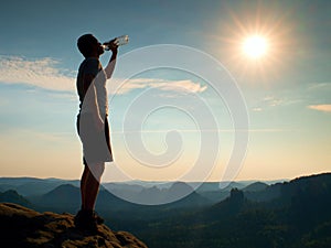 Thirsty hiker in black pants drinks from bottle of water. Sweaty tired tourist on the peak of sandstone rocky park Saxony Switzerl