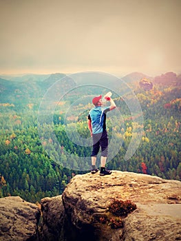 Thirsty hiker in blue and black sportswear drinking water from plastic bottle. Sweaty tired tourist