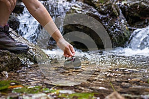 Thirsty hiker scoops fresh water into cup from stream in mountains