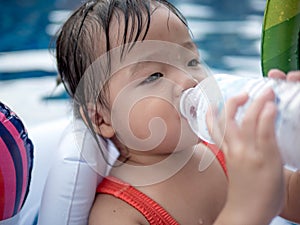 Thirsty kid girl refreshing herself and drinking water form plastic bottle in the pool