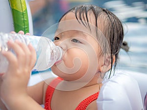 Thirsty kid girl refreshing herself and drinking water form plastic bottle in the pool