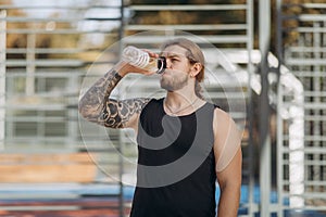Thirsty man drinking sports cocktail from bottle during bodybuilding training. Athlete man drinking water from sport