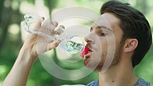 Thirsty man drinking water from bottle in summer park. Portrait of sport man