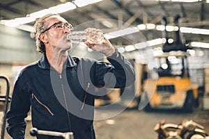 Thirsty senior male staff worker drinking water refreshing from tired hard work in hot workplace