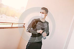 Thirsty sports man in face mask drinking water on balcony