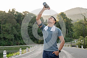A thirsty, tired Asian man is drinking pouring water from a bottle on his face after a long run