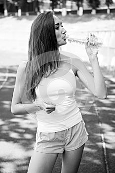 Thirsty woman drink water from bottle on stadium. Drinking water after training and workout. Thirst and dehydration