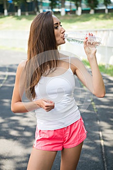 Thirsty woman drink water from bottle on stadium. Drinking water after training and workout. Thirst and dehydration. Refreshment a