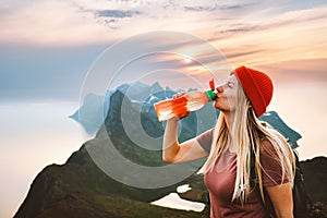 Thirsty woman drinking water with reusable plastic bottle on mountain summit girl traveling in Norway