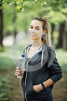 Thirsty woman drinking water to recuperate after jogging in city park