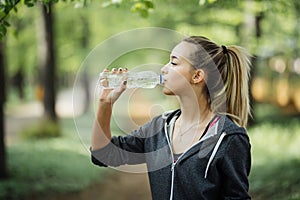 Thirsty woman drinking water to recuperate after jogging in city park